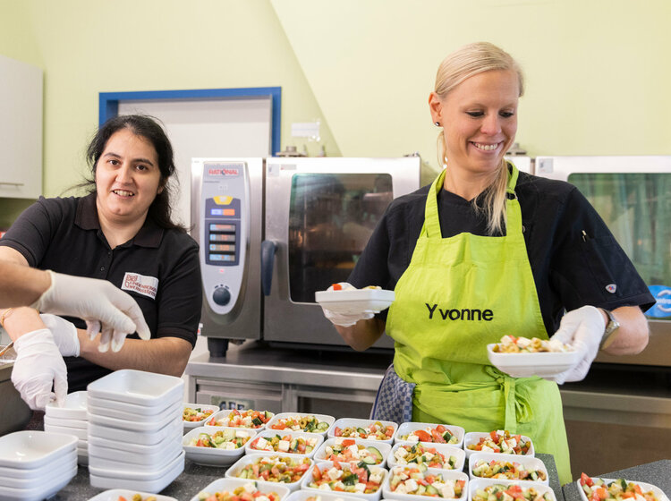 Zwei Frauen geben Schälchen mit Salat in einer Cafeteria aus