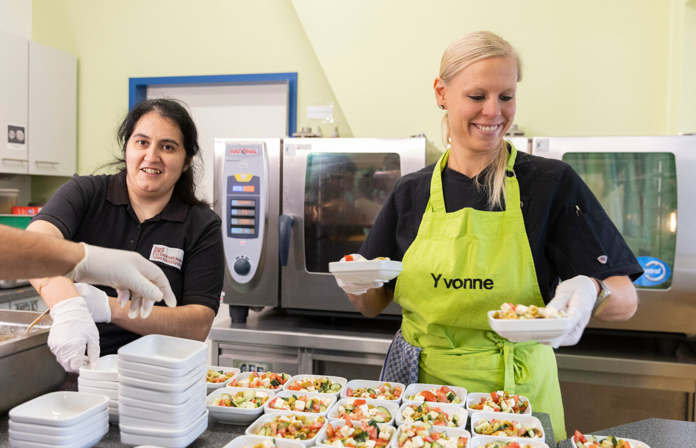 Zwei Frauen geben Schälchen mit Salat in einer Cafeteria aus