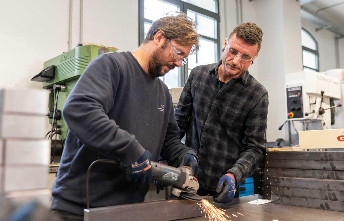 Zwei Männer bearbeiten ein Metallteil mit einer Flex