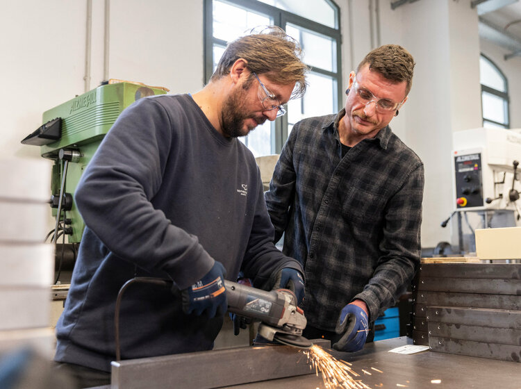 Zwei Männer bearbeiten ein Metallteil mit einer Flex