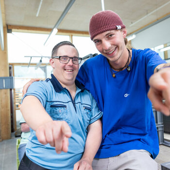 Ein Mitarbeiter der Lebenshilfe Lindau und ein Klient zeigen in die Kamera