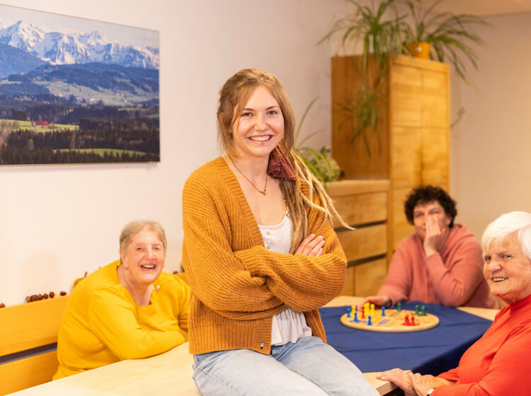 Eine Frau mit Dreadlocks und ältere Frauen sitzen gemeinsam am Esstisch