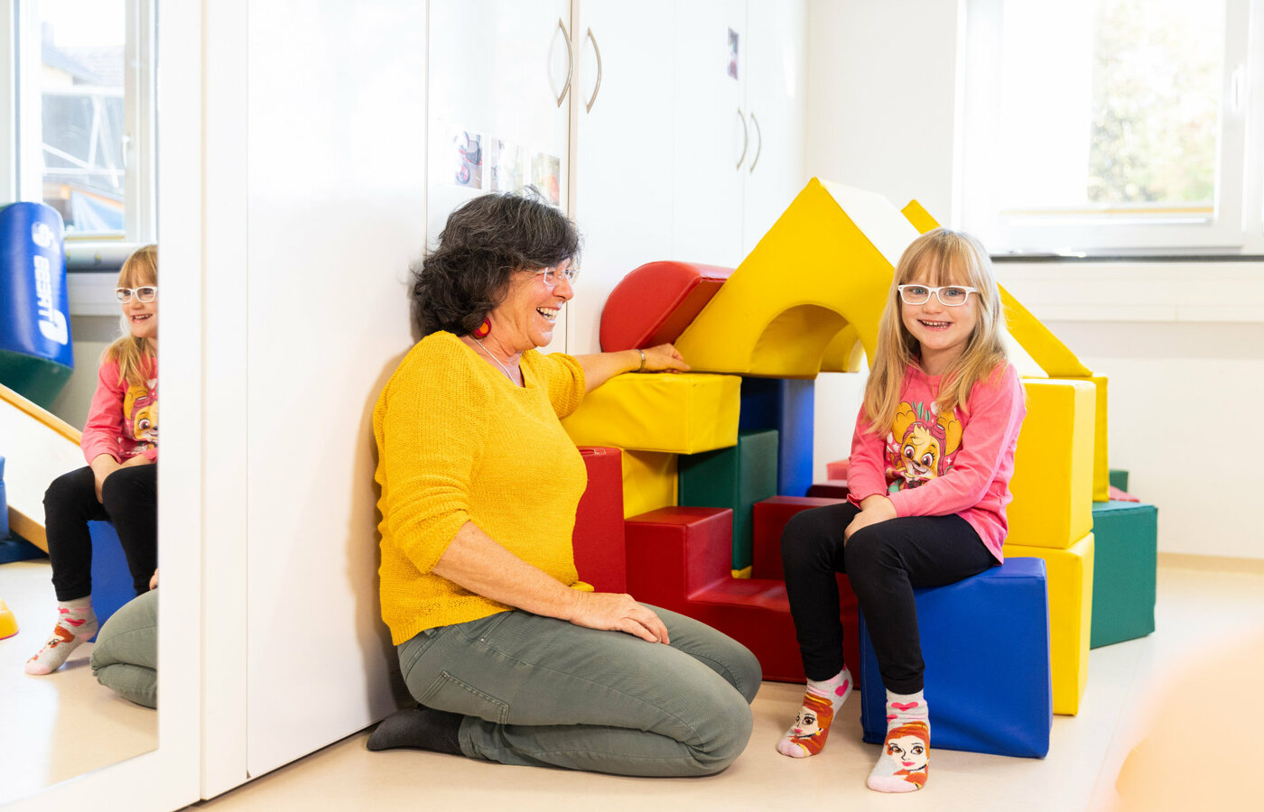 Eine Frau und ein Mädchen mit Brille neben einem Spielhaus