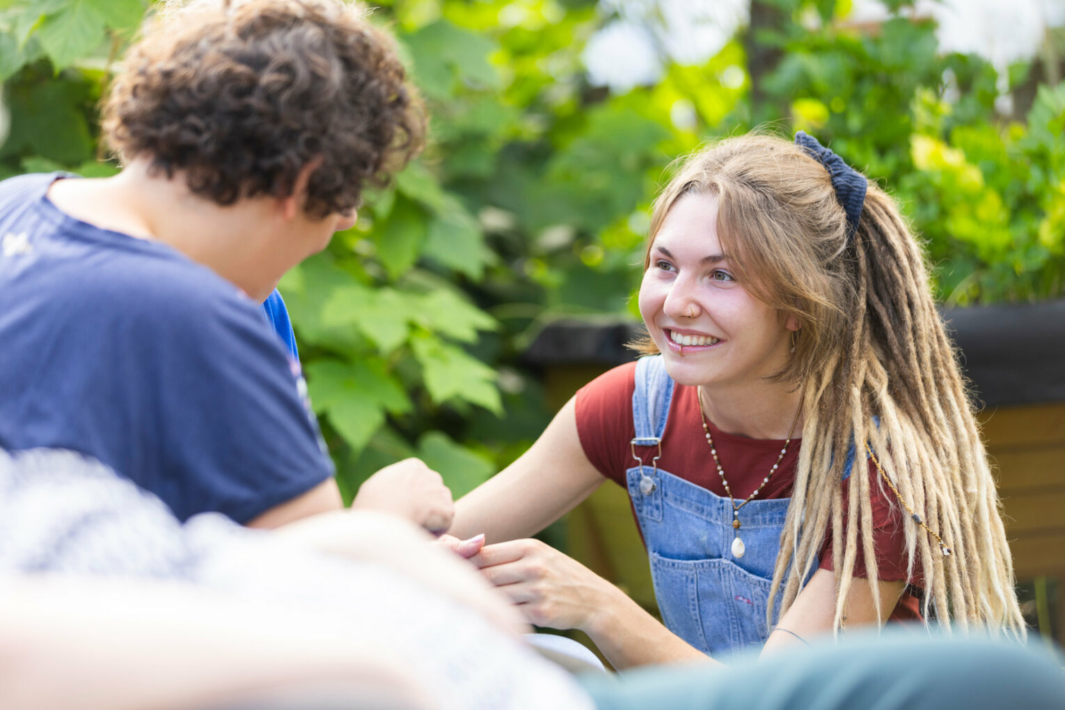 Eine junge Frau mit Dreadlocks unterhält sich mit einer Person im Freien