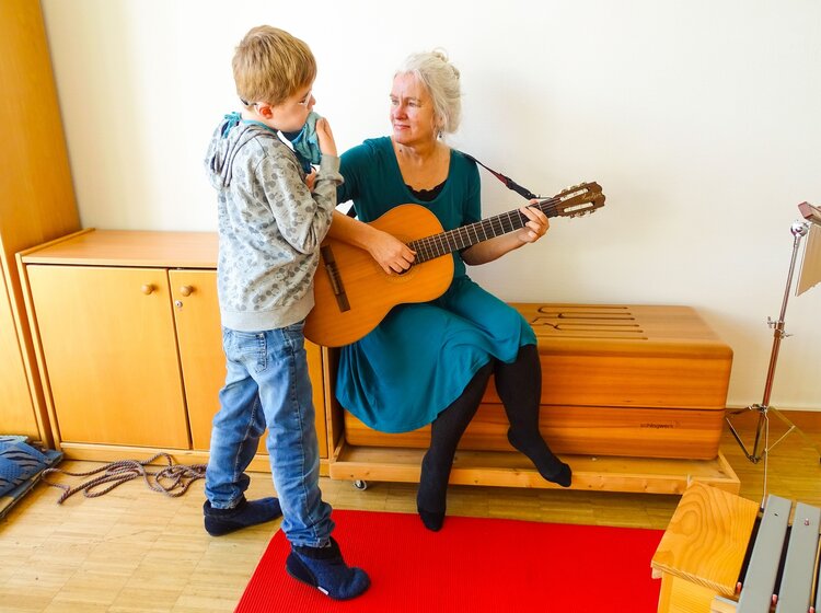 Eine Frau musiziert gemeinsam mit einem kleinen Jungen auf der Gitarre